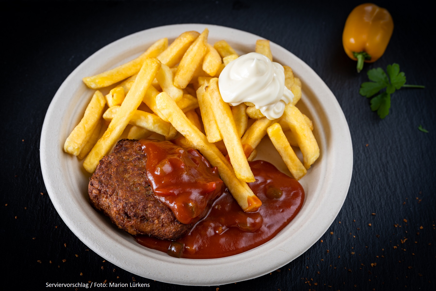 Eine Frikadelle mit Sauce und Pommes frites auf dem Teller.