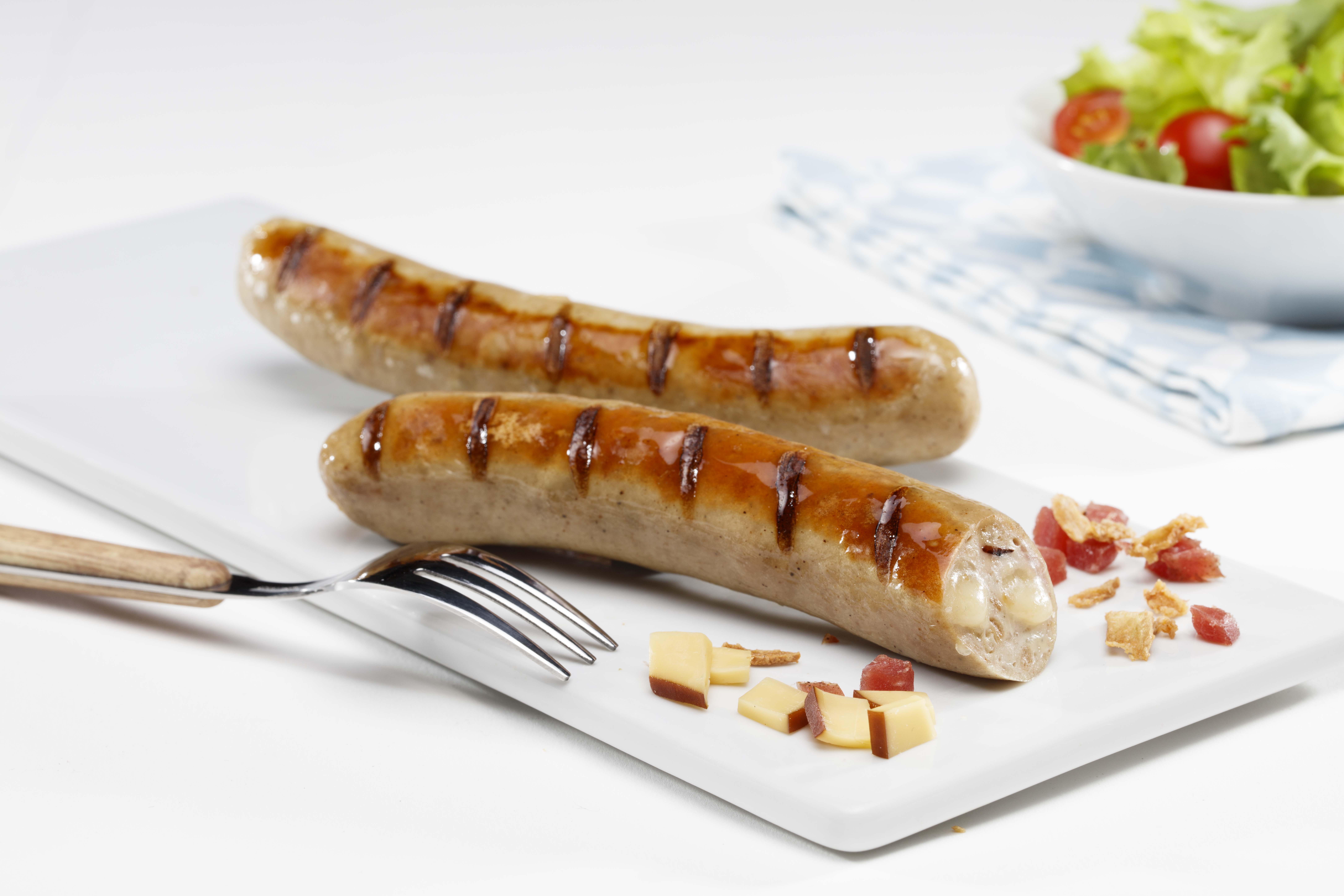 Zwei gebratene Bratwürstchen mit Gewürzen auf einem Teller. Ein Würstchen ist im Anschnitt zu sehen.