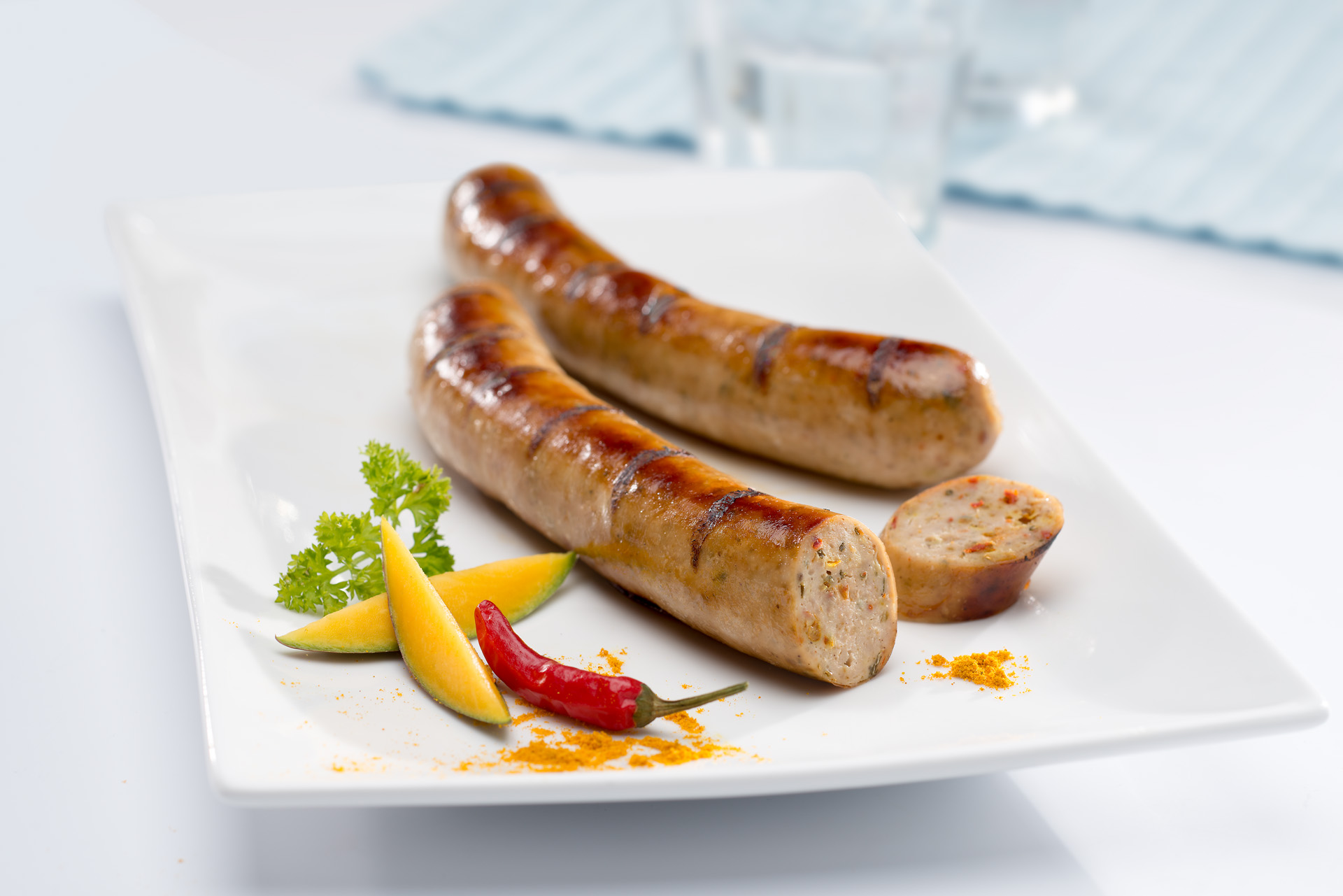 Zwei Bratwürste auf Teller mit Gewürzen. Eine Bratwurst ist angeschnitten.