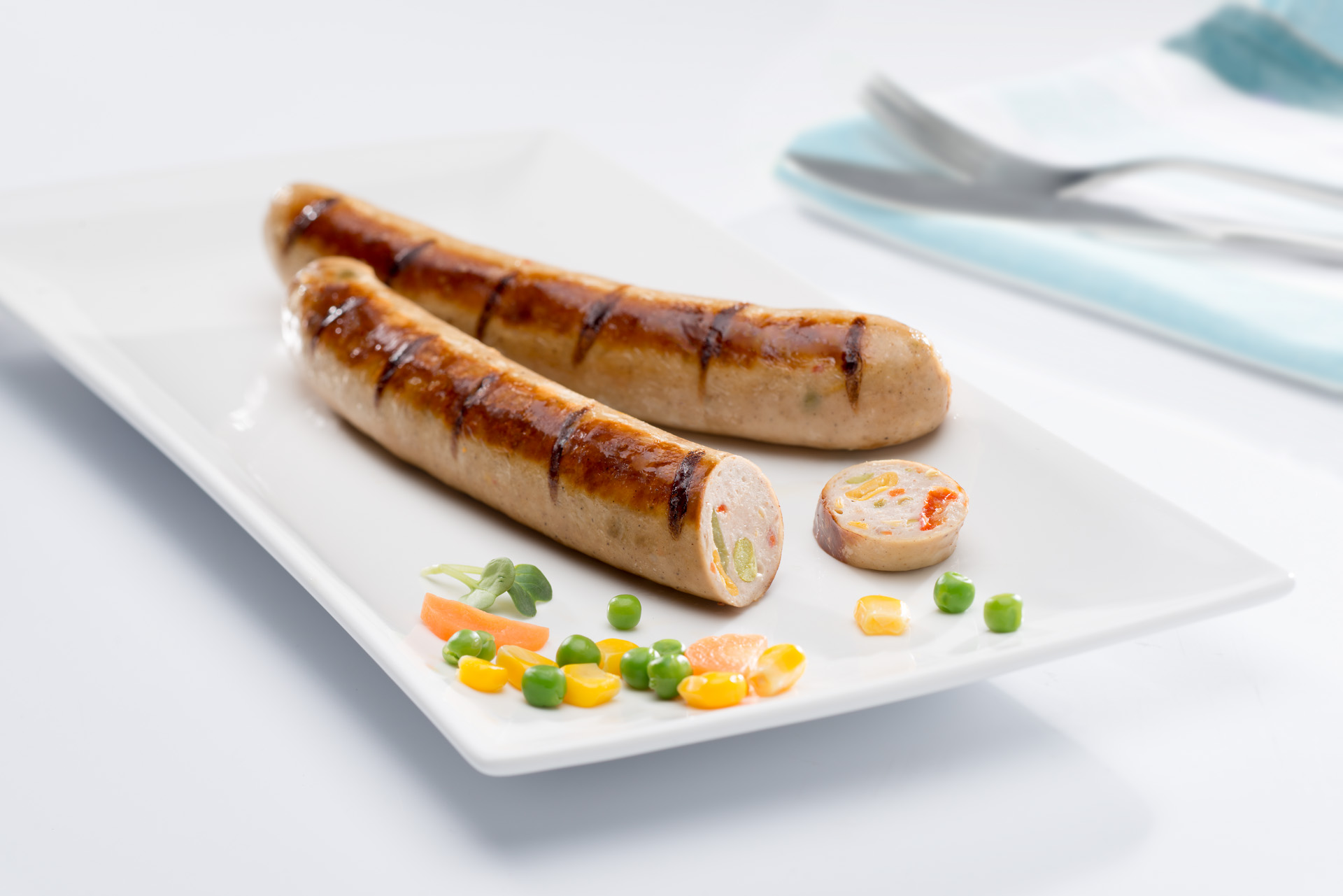 Zwei gebratene Bratwürste auf einem Teller mit Gemüse. Eine Wurst ist angeschnitten.